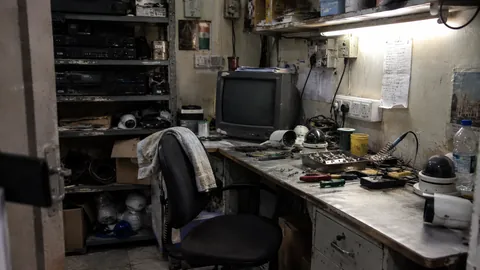 An old workshop bench with a monitor, hand tools and stripped-down equipment laid out across it.