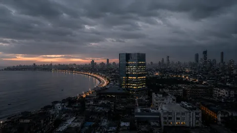 The Mumbai seafront at dusk from above, the curve of the bay lit and the towers of the business district behind it.