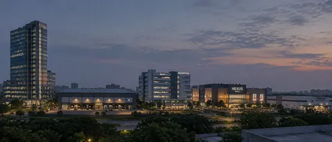 A waterfront campus at dusk, low lit buildings along the shoreline and the city beyond the water.