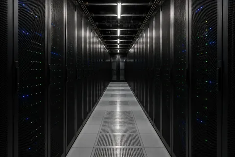 An aisle between two runs of black server cabinets, indicator lights receding down a raised floor.
